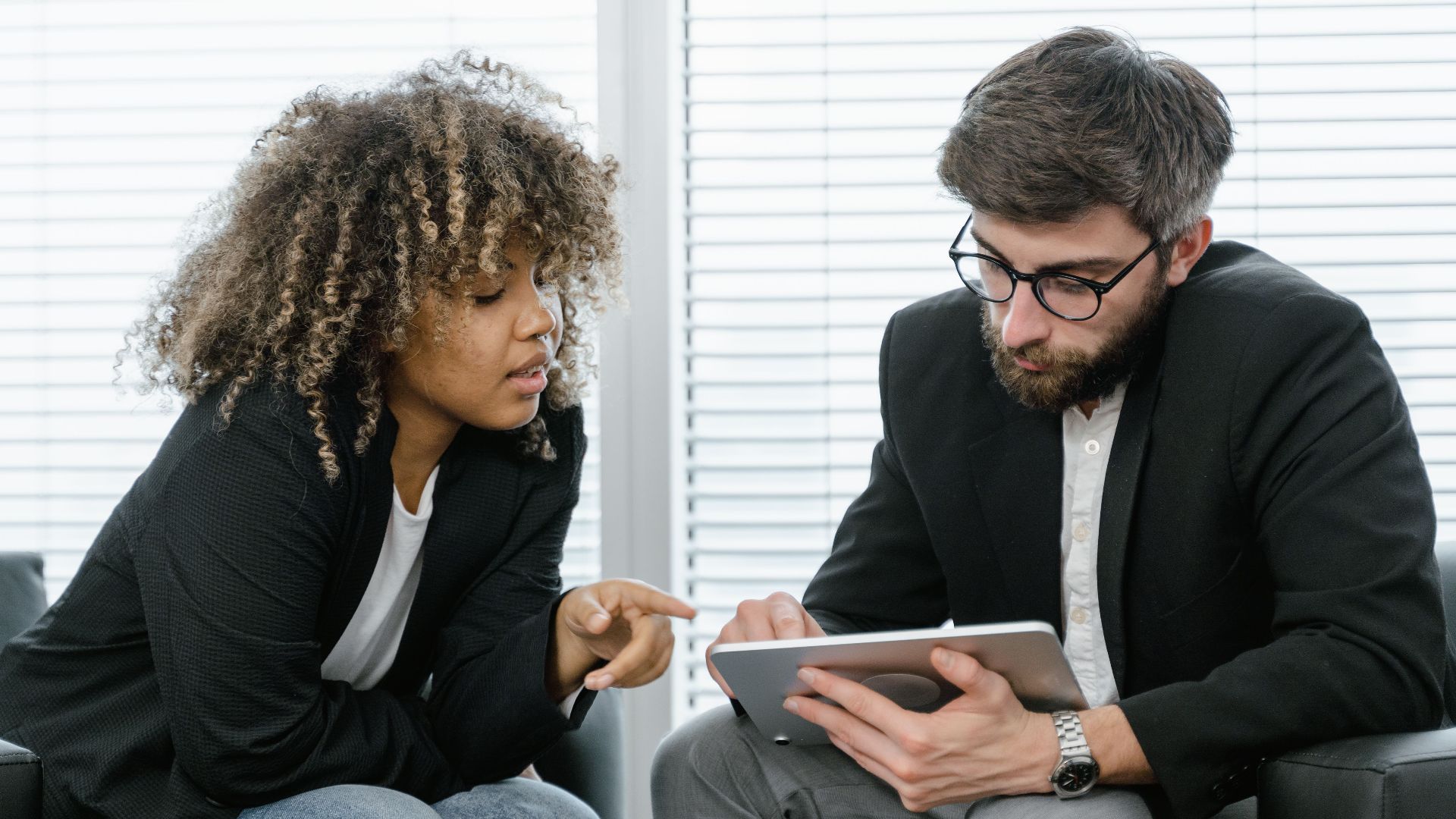 Two colleagues in a business setting discussing ideas using a tablet for planning.