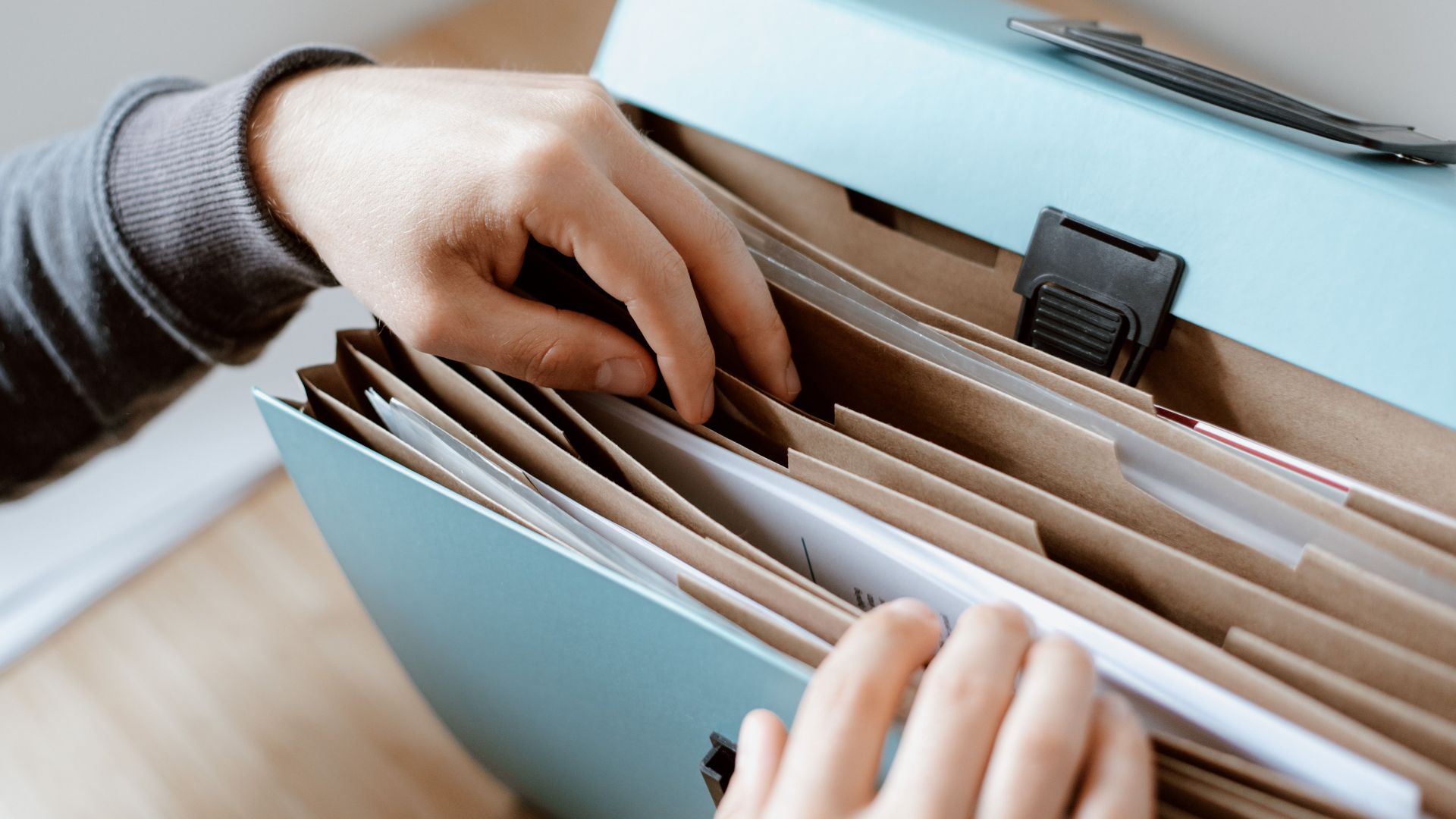 Crop unrecognizable person selecting document in opened briefcase for documents placed on wooden table