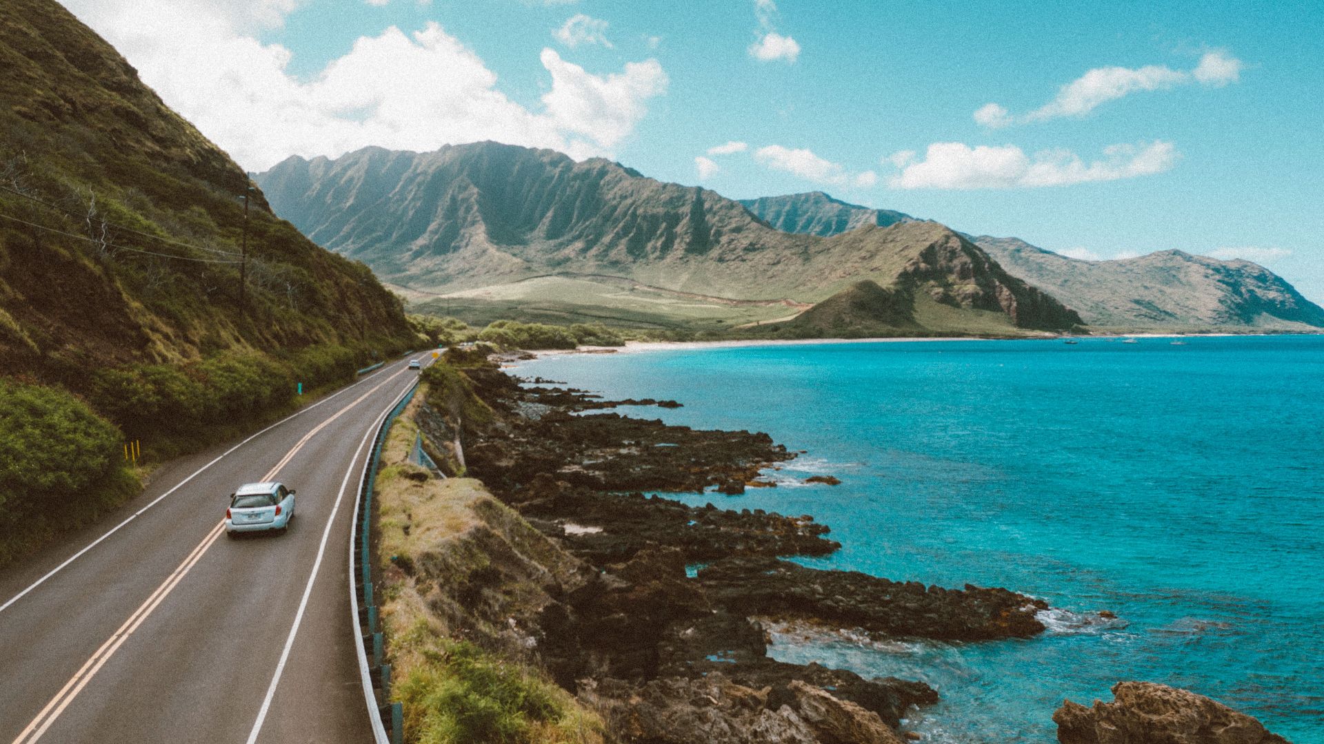 A stunning aerial view of a coastal road in Hawaii, featuring ocean and mountains.