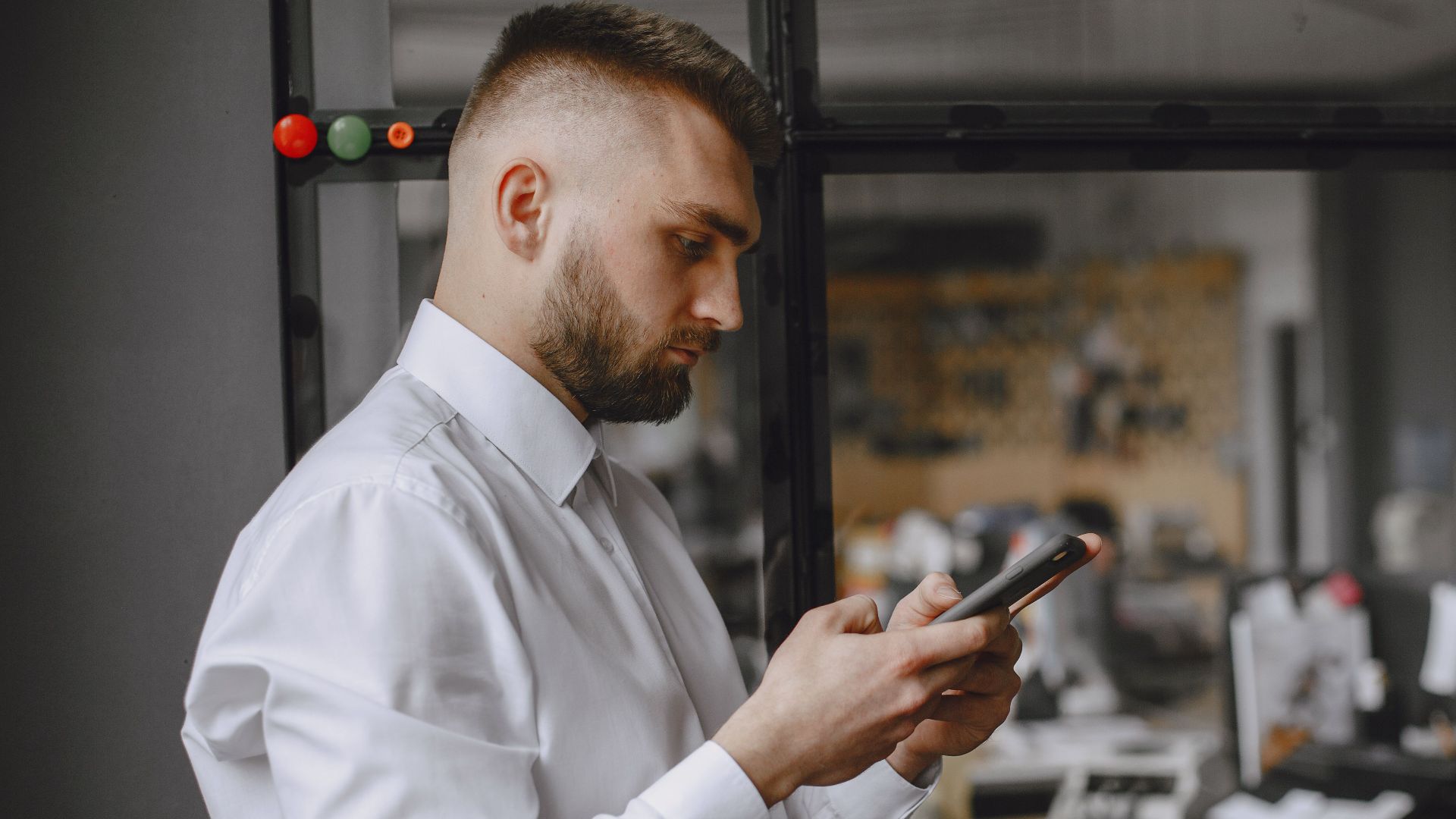 Businessman in white shirt using phone in office, showcasing modern technology and workplace focus.