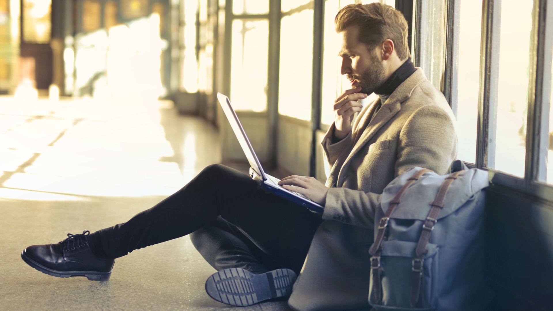 Young man sitting indoors at an airport using laptop. Ideal for remote work themes.