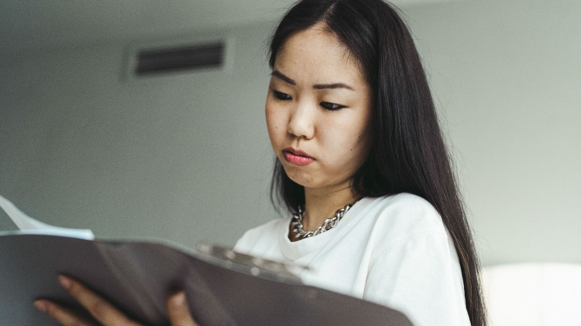 Asian woman in casual attire examining paperwork with concentration indoors.