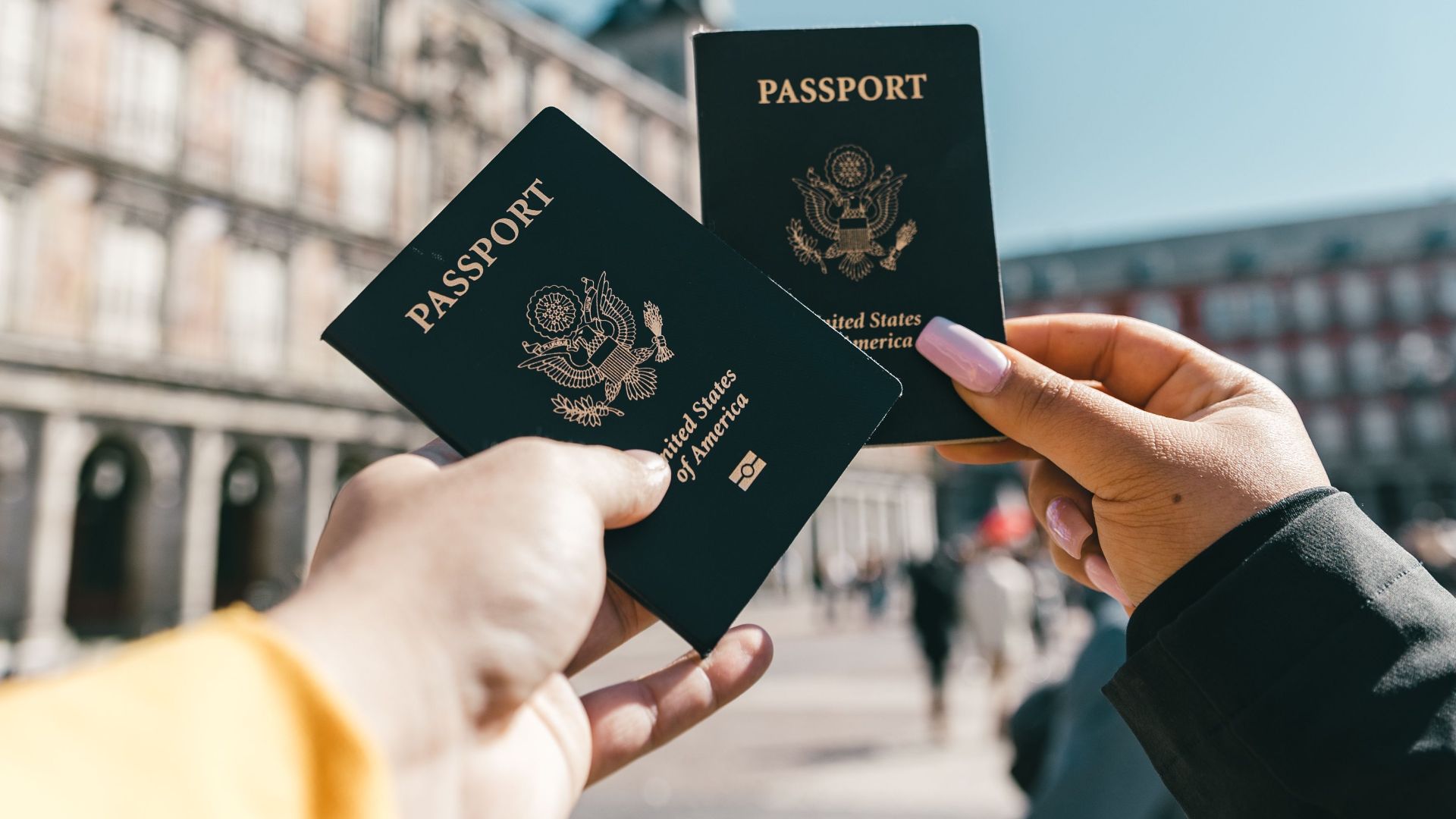 Crop unrecognizable travelers in casual clothes demonstrating passports of United States of America standing on square in historical city district