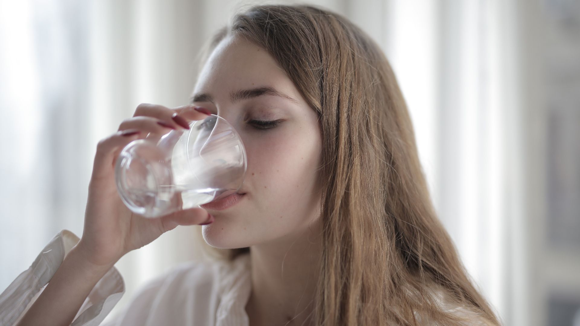 A woman enjoying a refreshing glass of water indoors during the day.