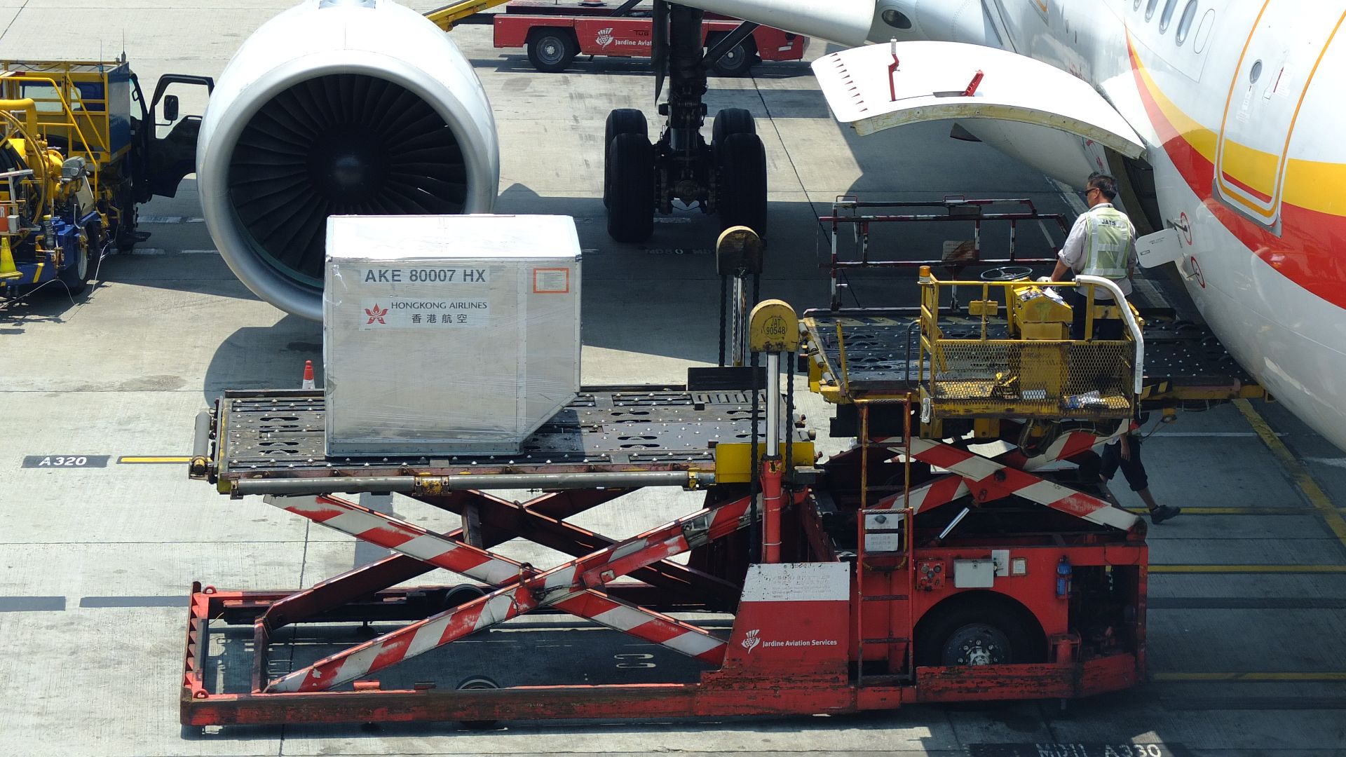 Photo showing a ULD loader lifting a ULD from apron dollies level to aircraft cargo bay level. Unit Load Device (ULD) is standardized size air cargo container. All are apron Ground support equipment.