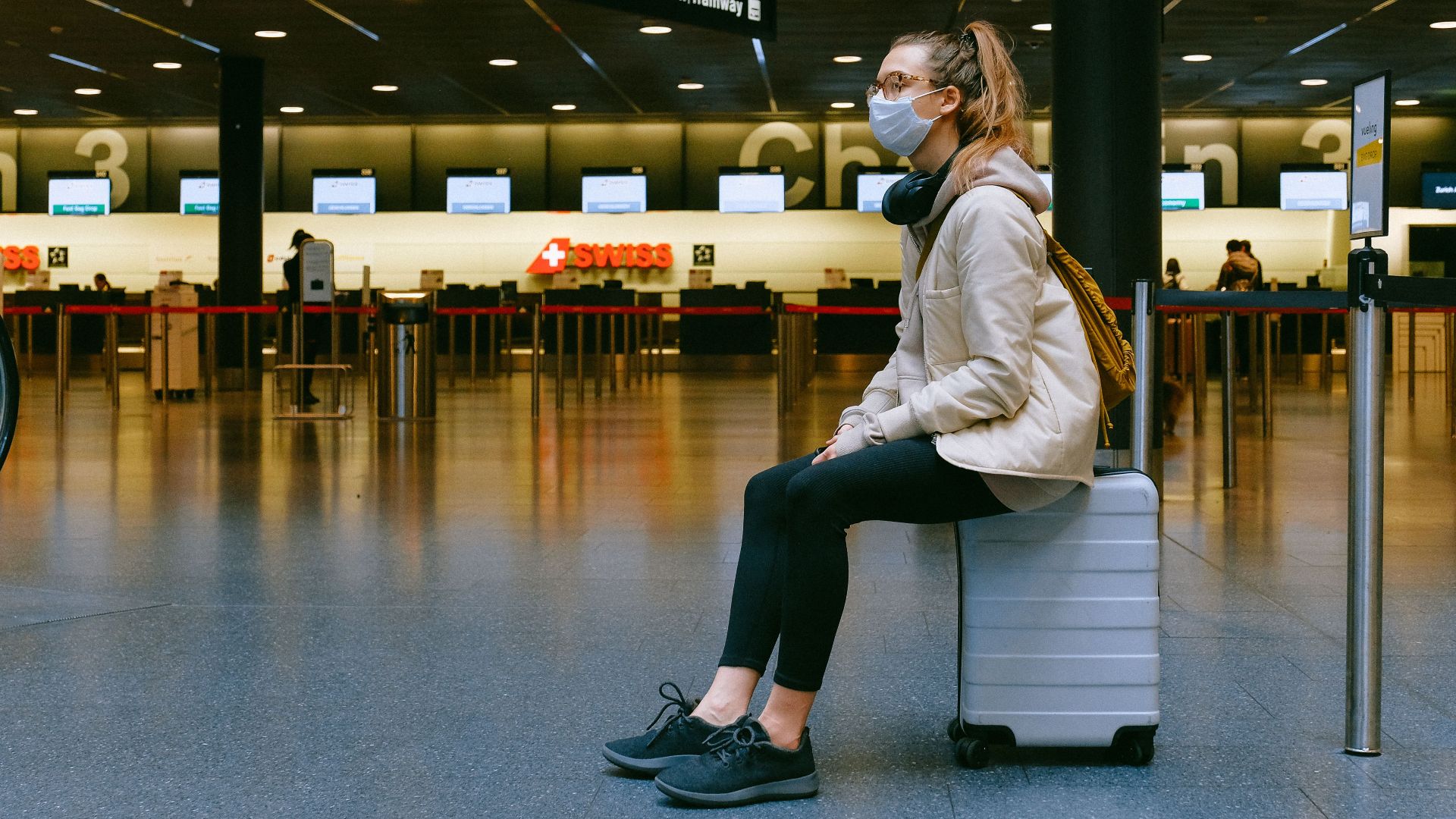 A woman wearing a face mask sits on luggage in an airport terminal amid the pandemic.