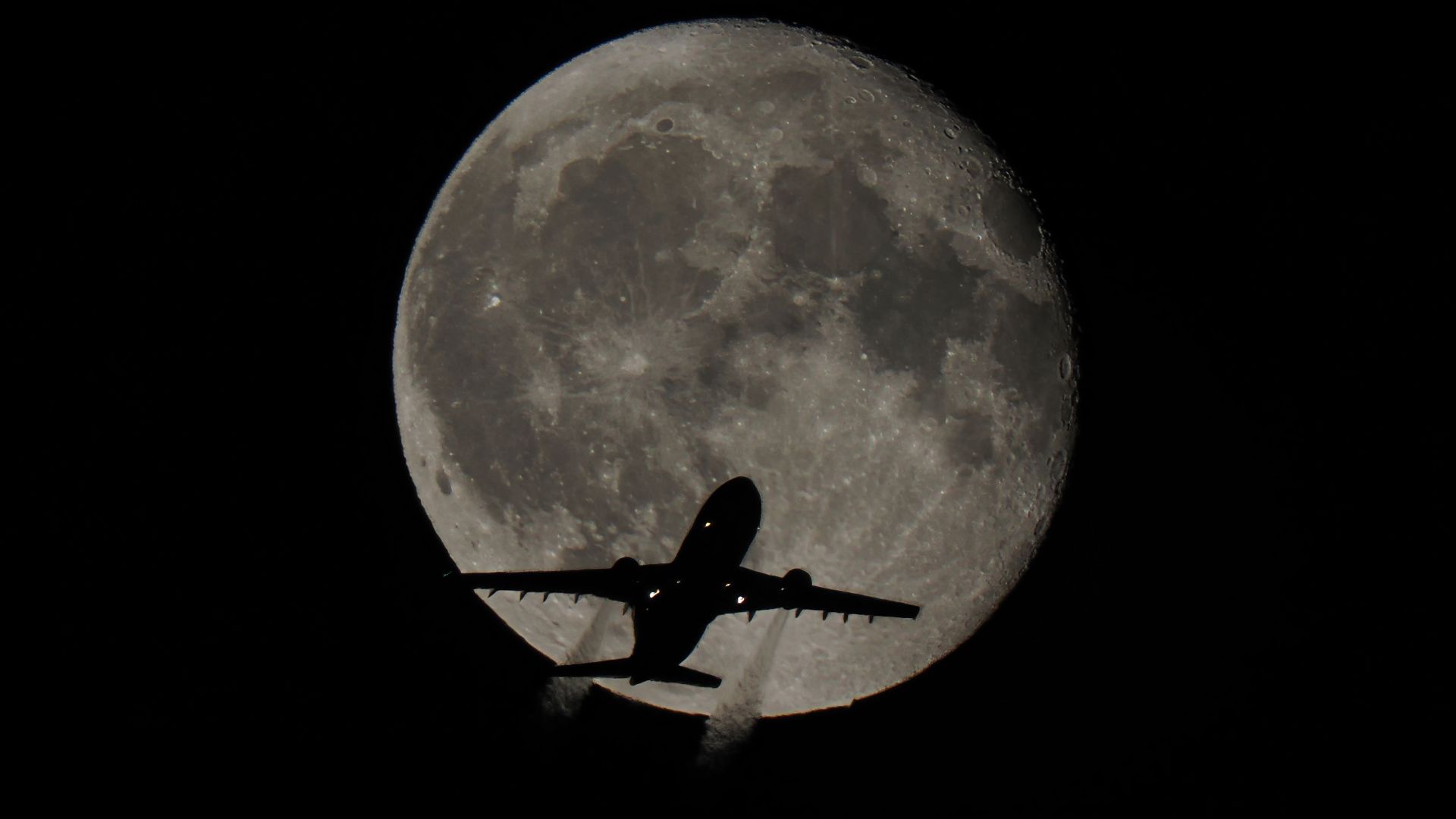 A striking view of an airplane silhouetted against the full moon, captured at night.