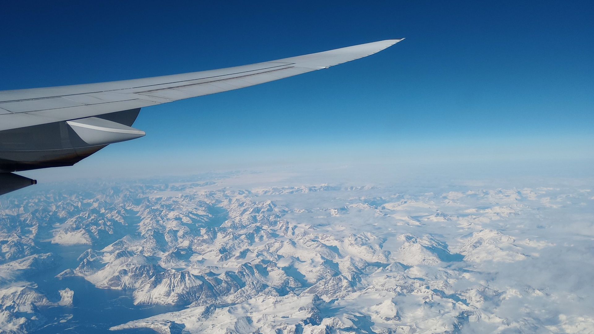 Stunning aerial shot of Greenland's snow-covered landscape with an airplane wing in view.