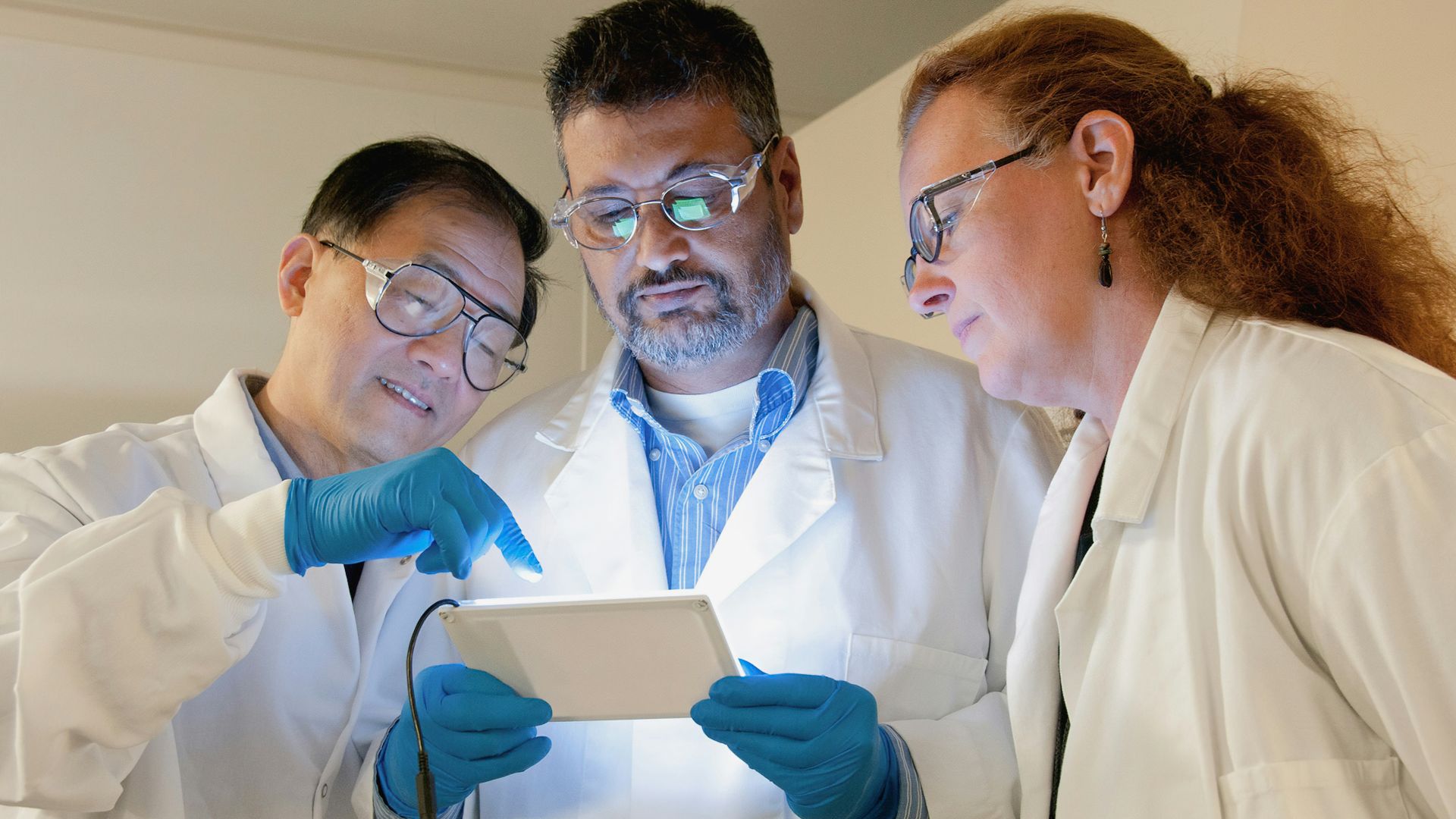 three people in lab coats looking at a tablet