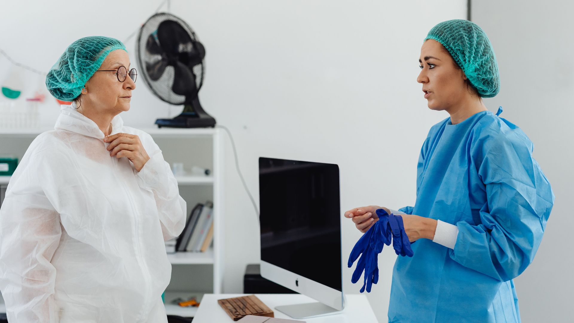 Two female healthcare professionals in conversation wearing protective gear in a laboratory setting.