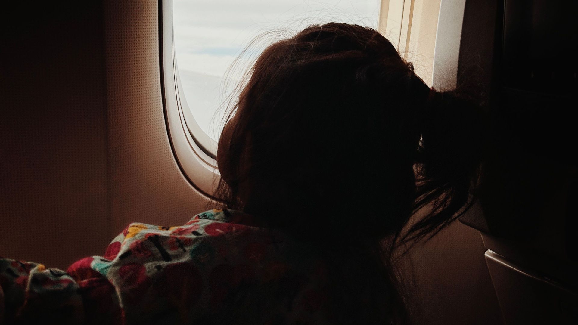 A child sits by an airplane window, gazing outside during a flight.