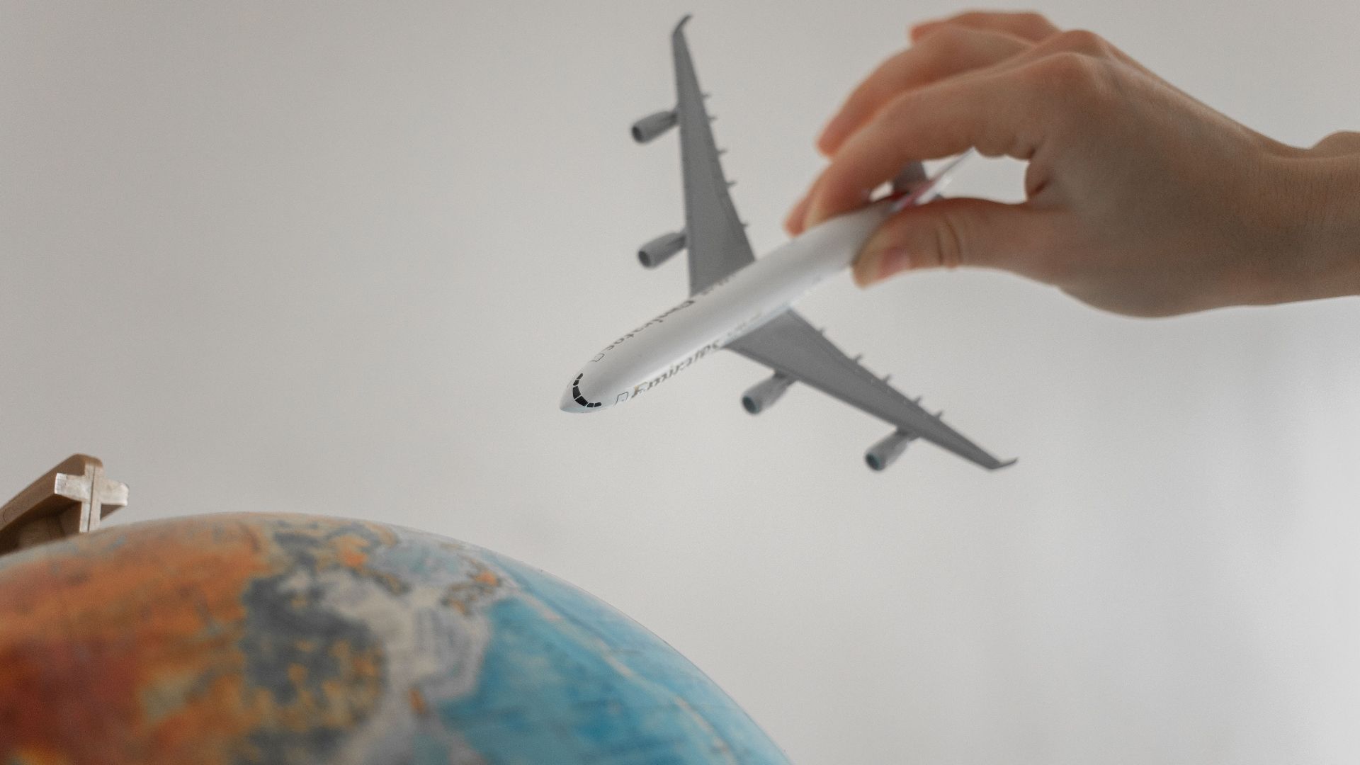 A hand holds a toy airplane above a globe, symbolizing travel and exploration.