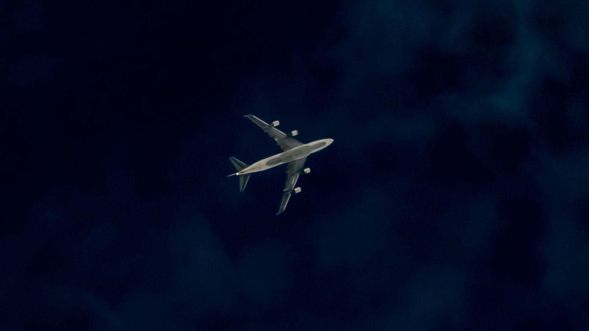 A commercial airplane captured mid-flight against a dark, moody sky.