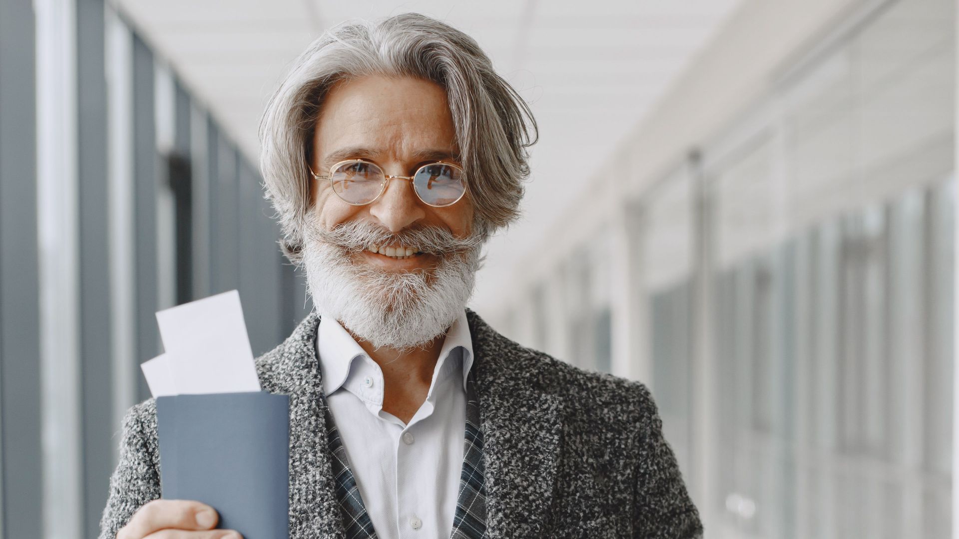 Elderly man in airport holding passport and luggage, smiling confidently at the camera.