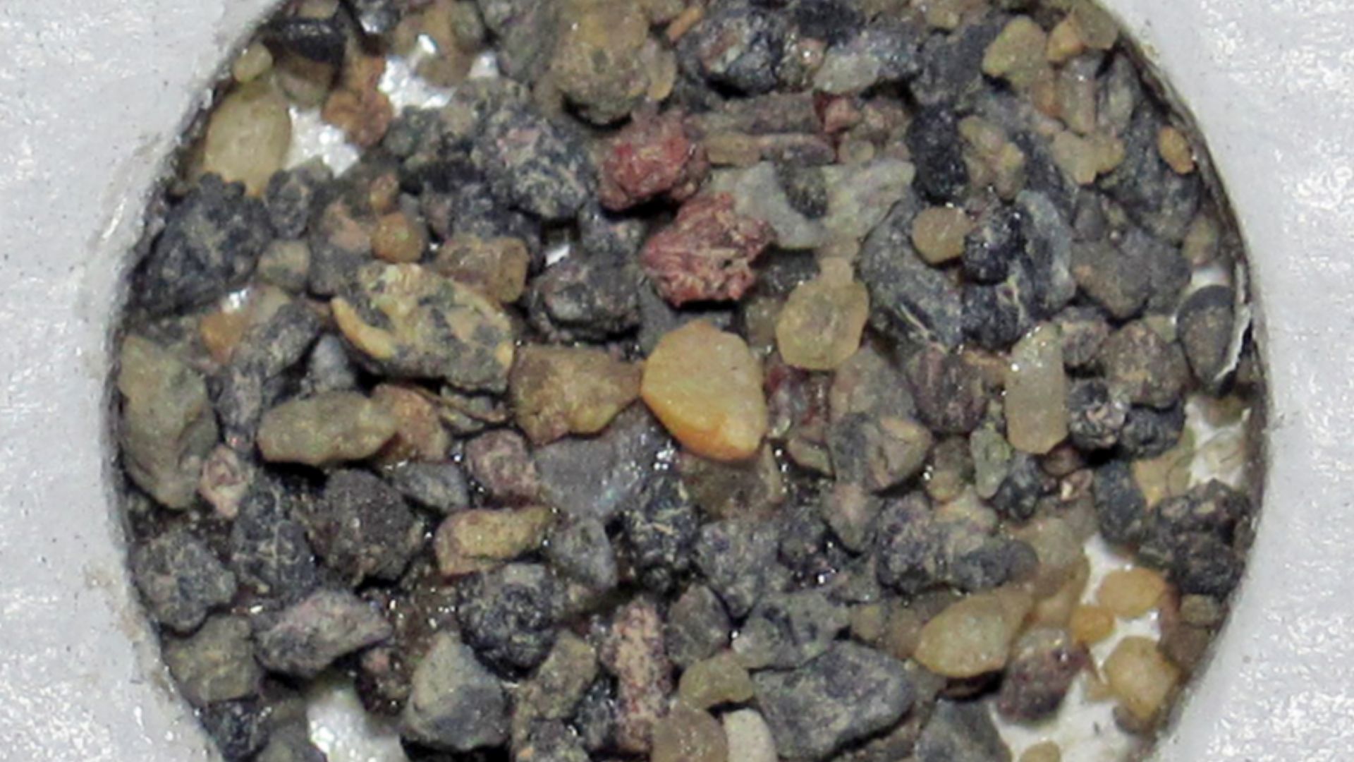 (circular holder is 1.0 centimeter in diameter)

Sediments are defined as naturally-occurring, loose grains of any composition or origin at the Earth's surface (although they also occur in cave passages).  Most sediments are lithogenous - they form by wea