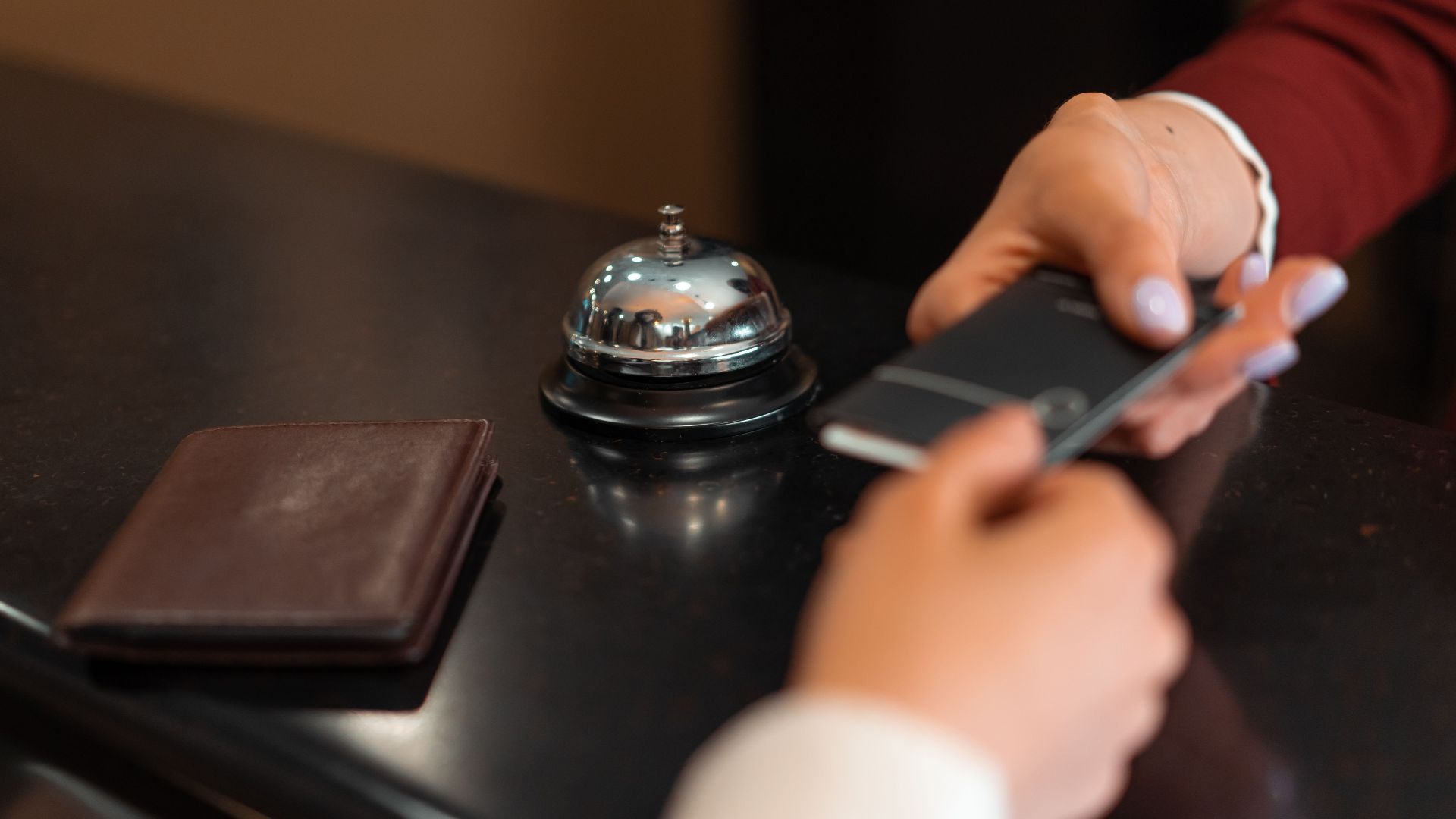 A close-up of a hotel check-in process with a smartphone and card transaction at the reception desk.