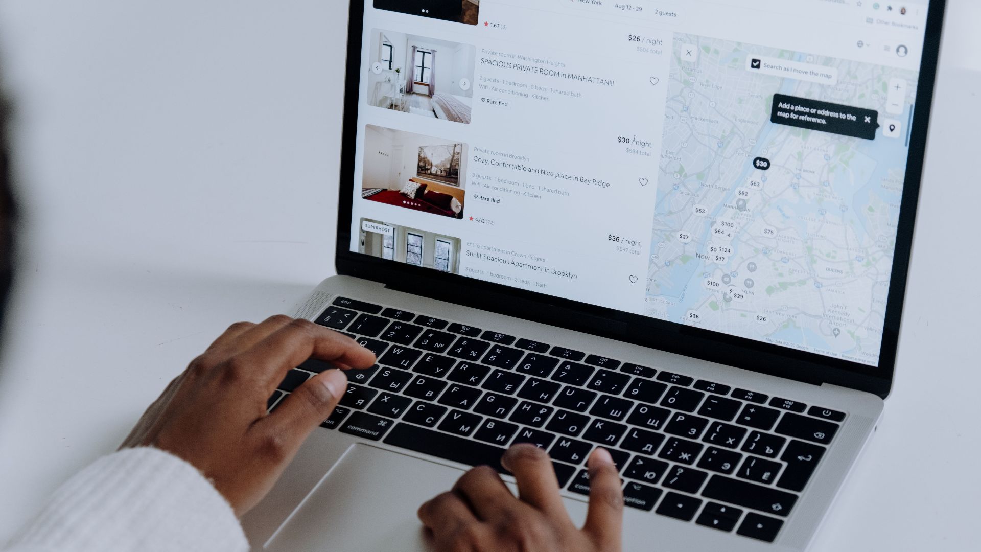 Hands typing on laptop searching Airbnb for accommodation options with map view.