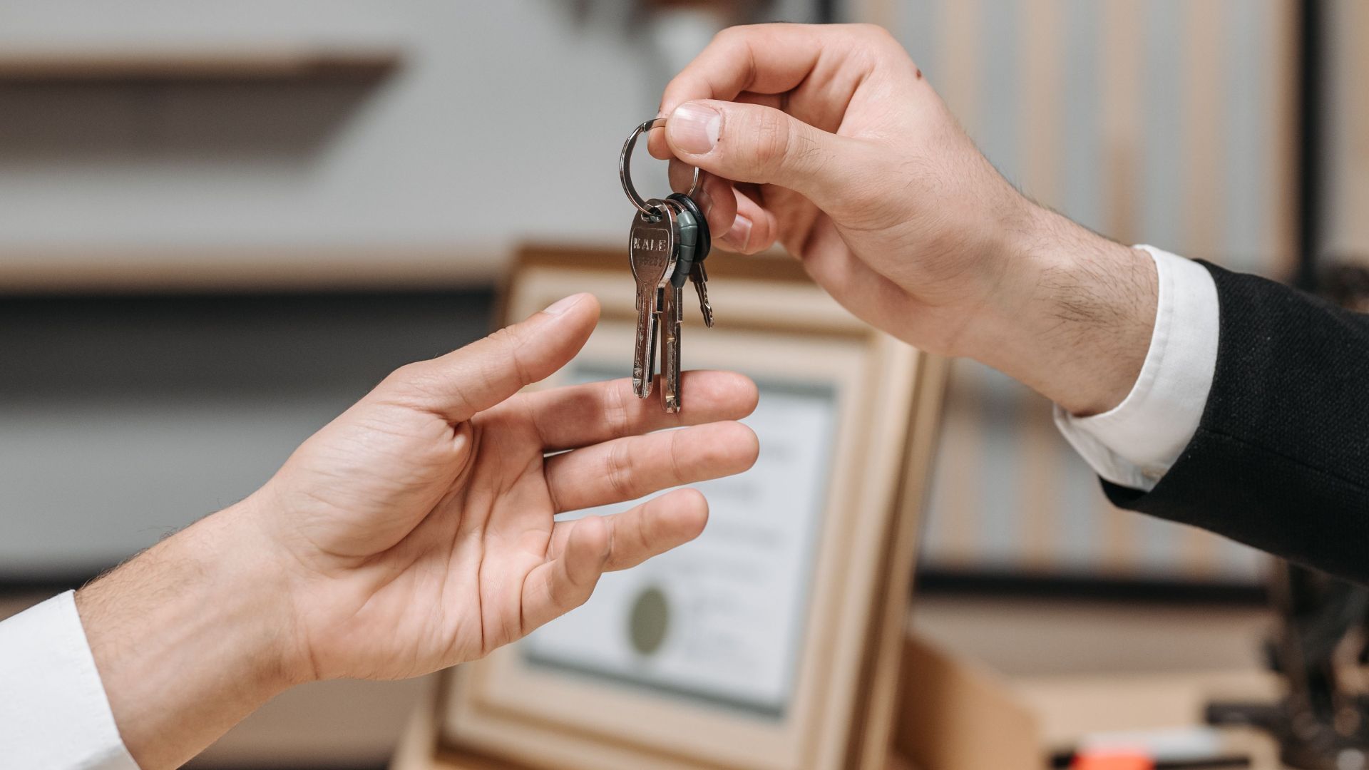 Detailed view of hands exchanging keys in a professional office environment, symbolizing real estate or business transactions.