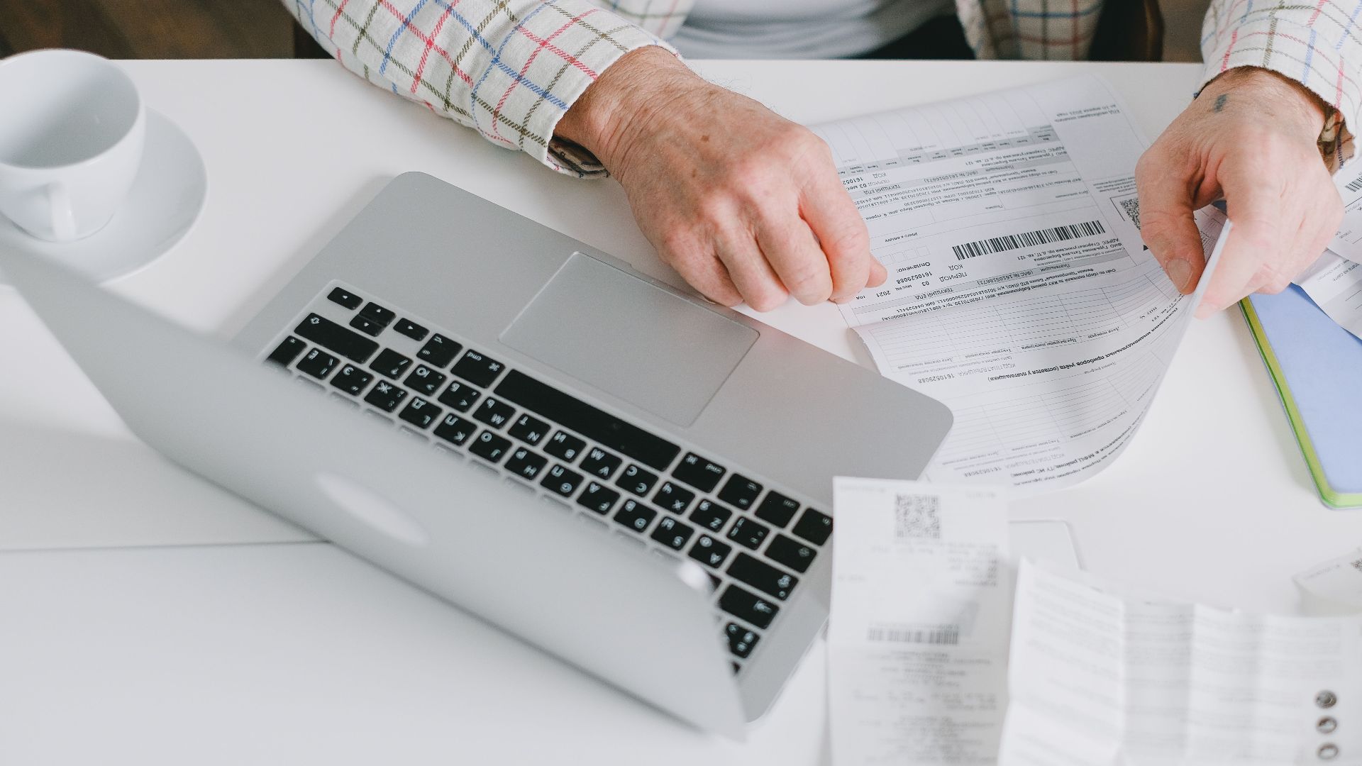 Close-up of hands organizing documents on a desk with a laptop.