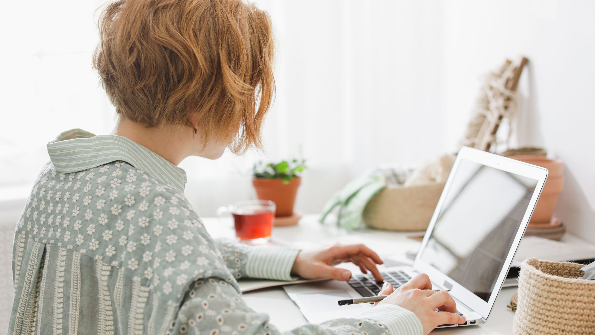 A woman working remotely in a bright, minimalist home office with a laptop.