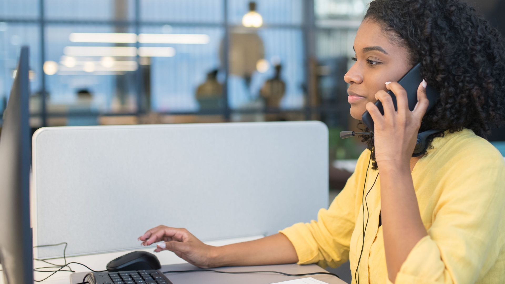 A young woman working in a modern call center environment, engaging in conversation via headset.
