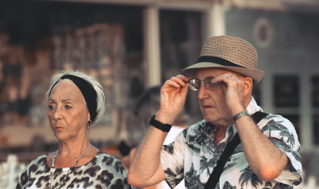 Elderly couple walking past a cafe in a Mediterranean town, enjoying a sunny day