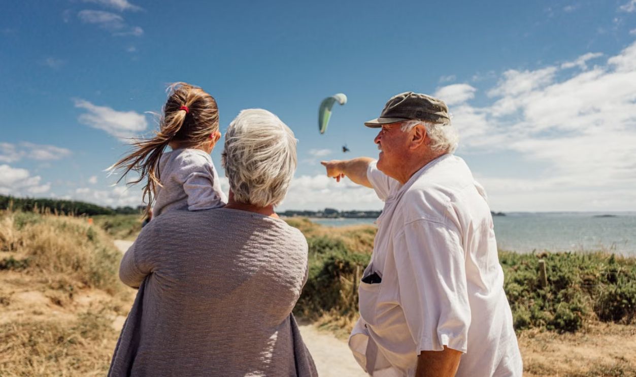Elderly couple with granddaughter watching the sea and a paraglider on a sunny day in Penestin, Brittany, France