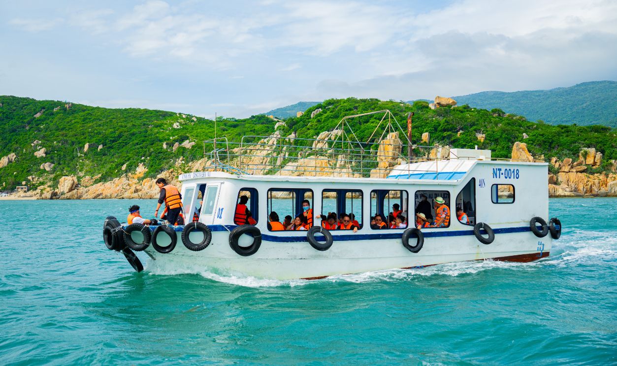 A boat filled with tourists in life jackets traverses vibrant turquoise waters along a lush, green coastline