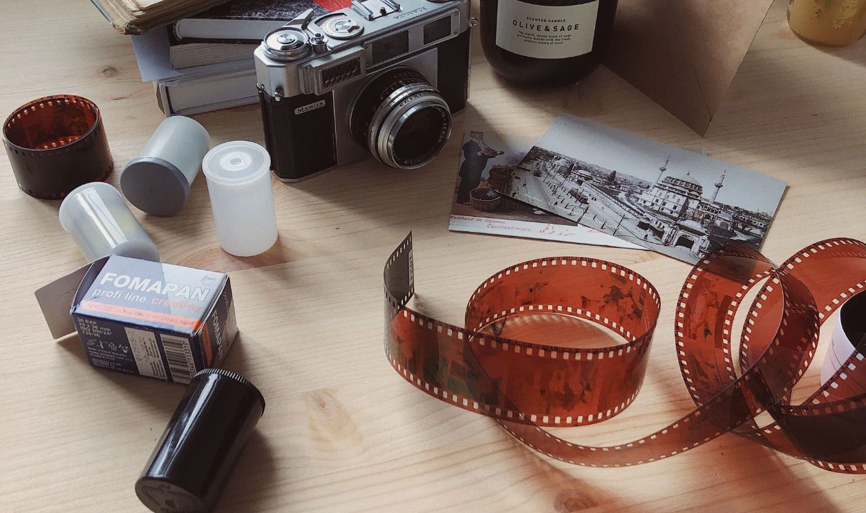 A cozy vintage setup with camera, films, and open book on a wooden desk, perfect for photography