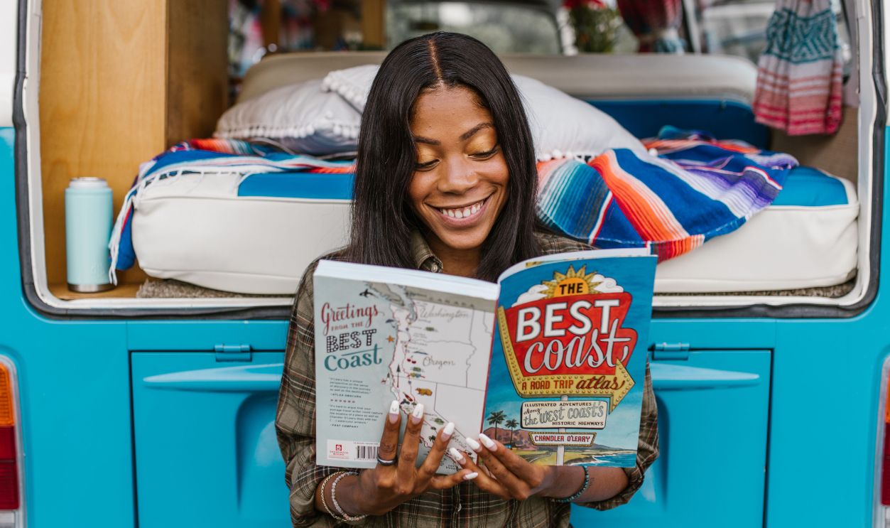 Woman enjoying a book while sitting on a colorful camper van, embracing travel