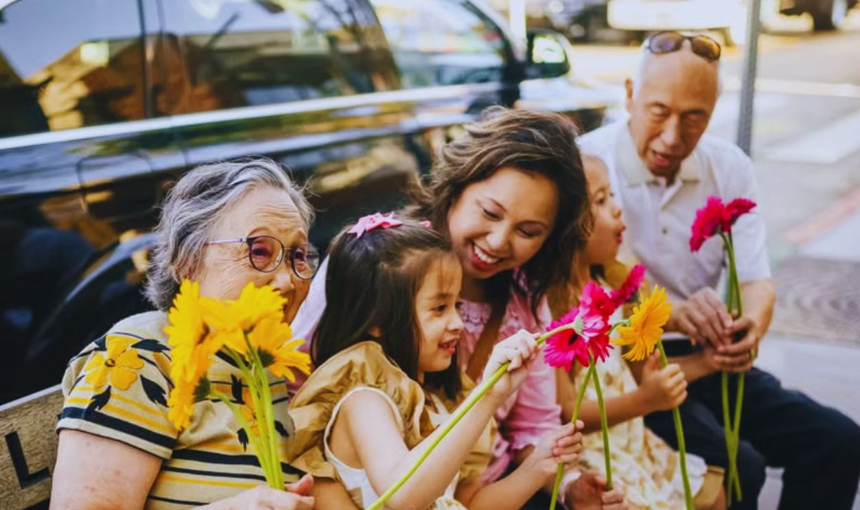 Happy multigenerational Asian family sitting together with flowers on a city bench, enjoying a sunny day