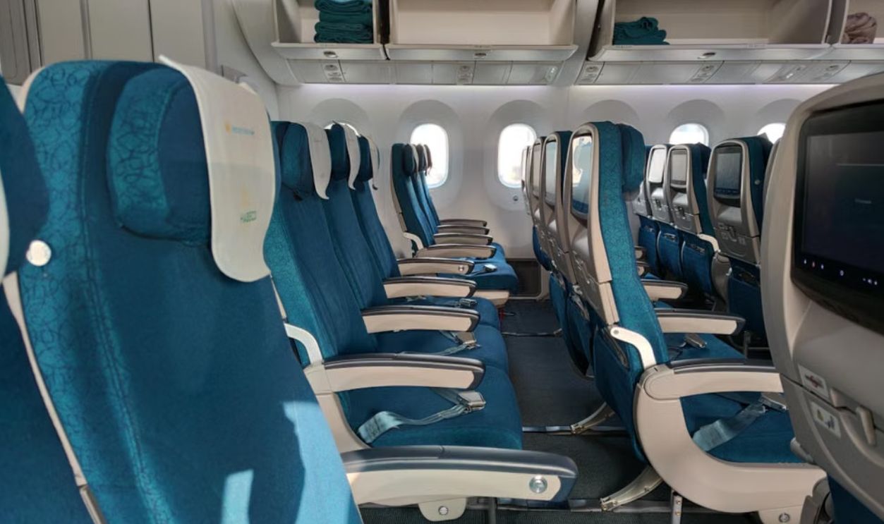A row of empty blue airplane seats in an economy class cabin on a sunny day