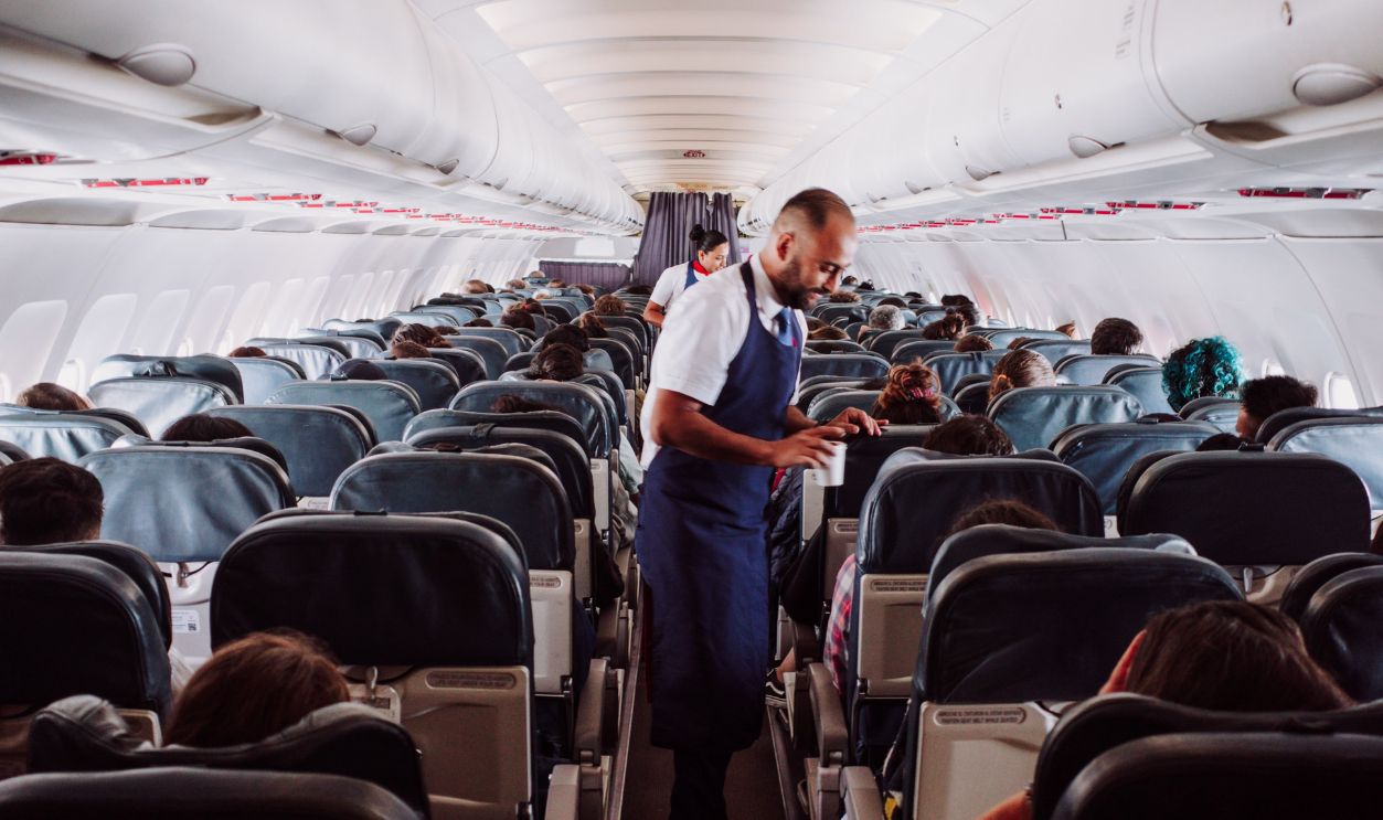 Flight attendant assists passengers in a crowded airplane aisle with rows of seats