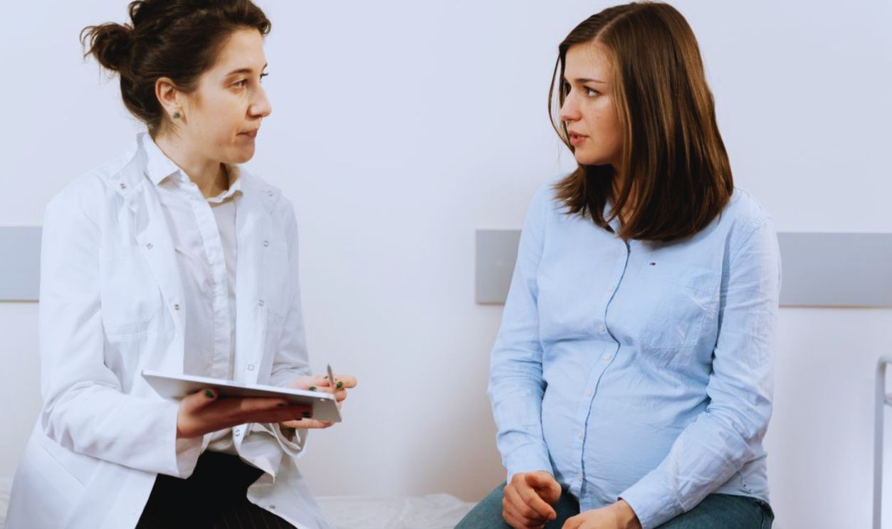 A pregnant woman consulting with a female doctor in a medical clinic setting.