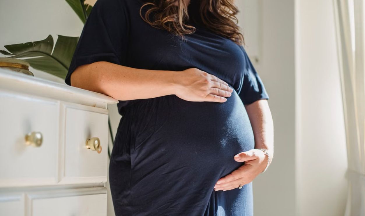A serene image of a pregnant woman standing indoors, embracing motherhood with calmness and anticipation