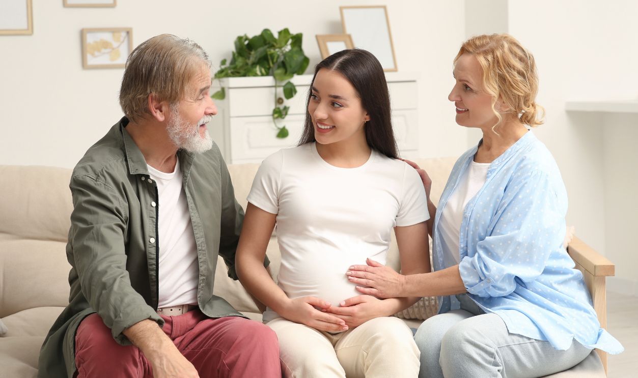 Happy pregnant woman spending time with her parents at home. Grandparents' reaction to future grandson