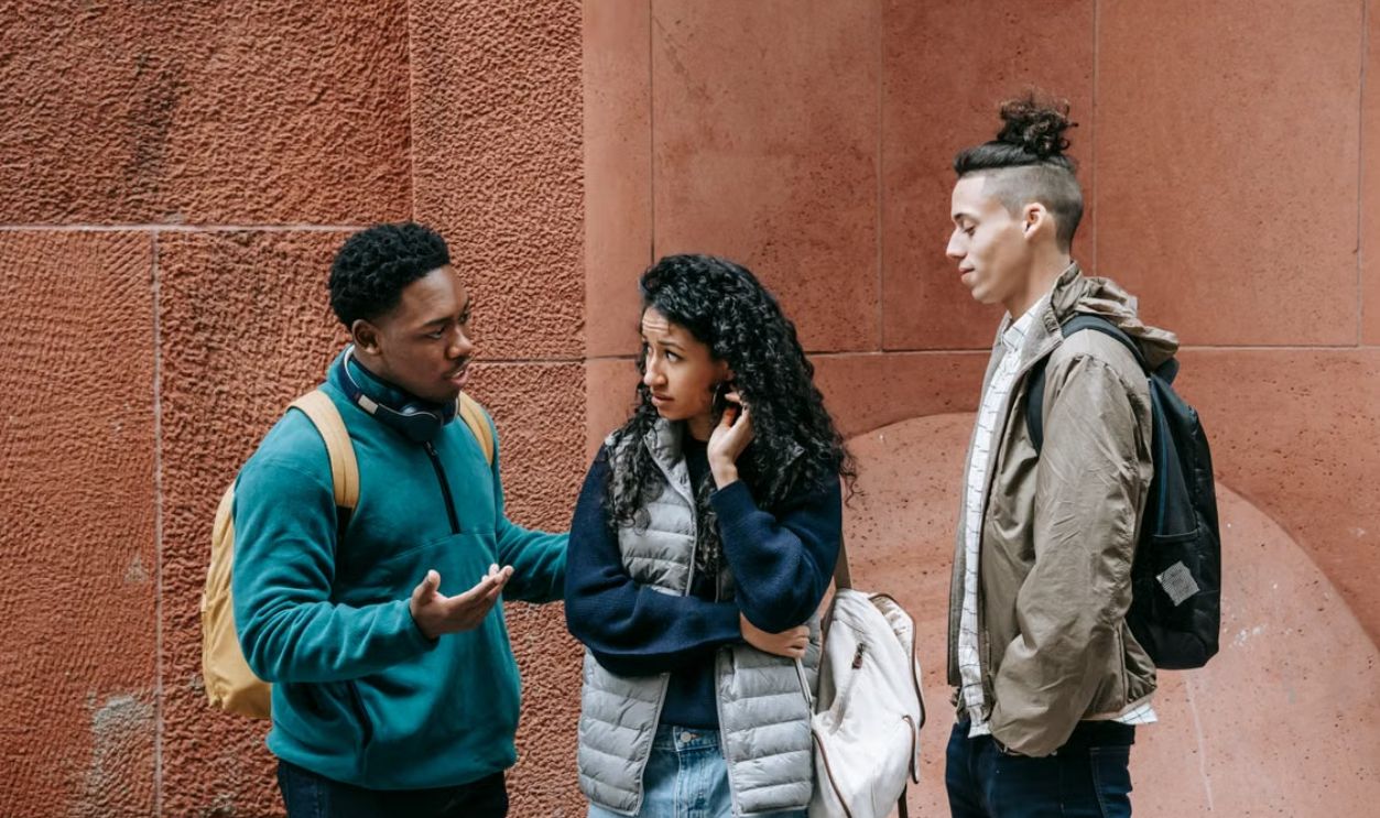 Three diverse students engage in a thoughtful discussion outdoors, embodying modern campus life.