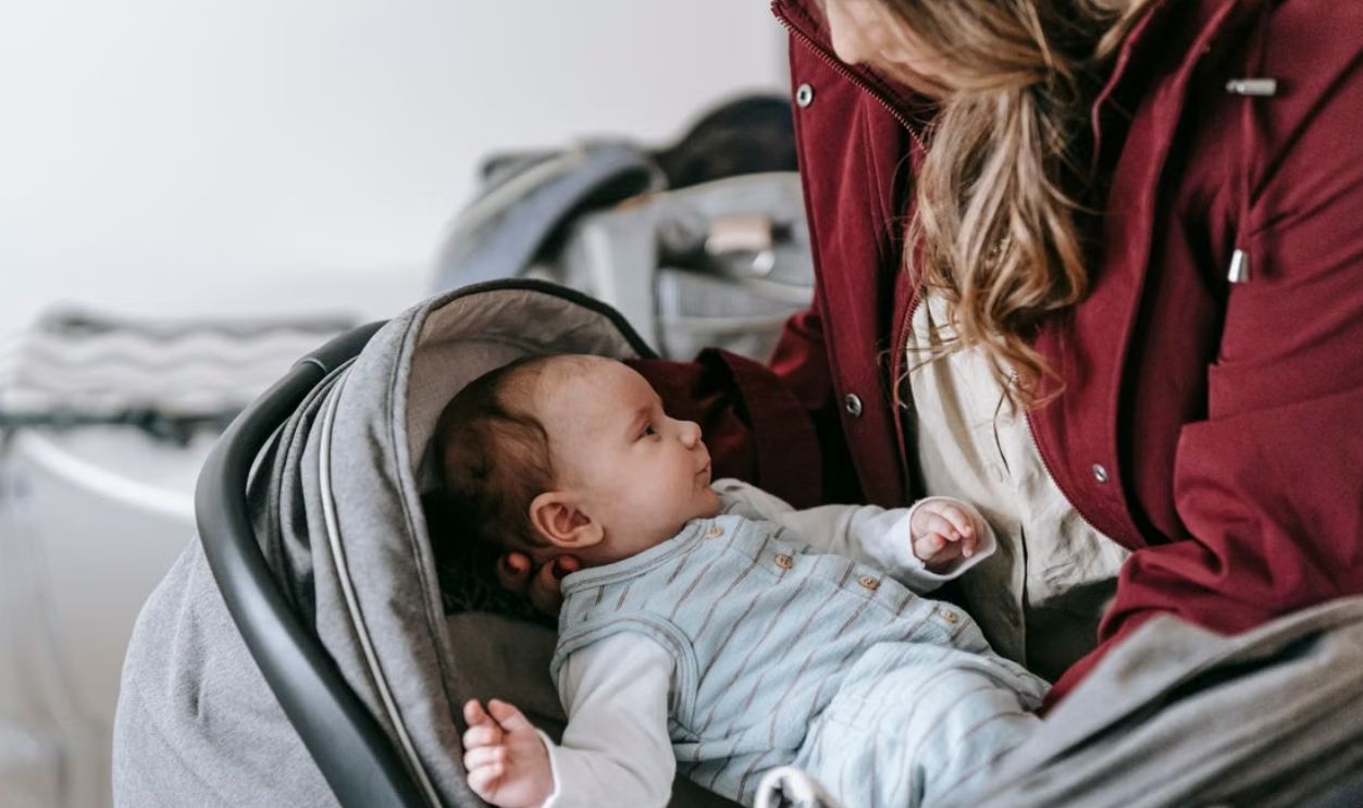 A loving mother gazes at her newborn in a stroller indoors, emphasizing care and tenderness