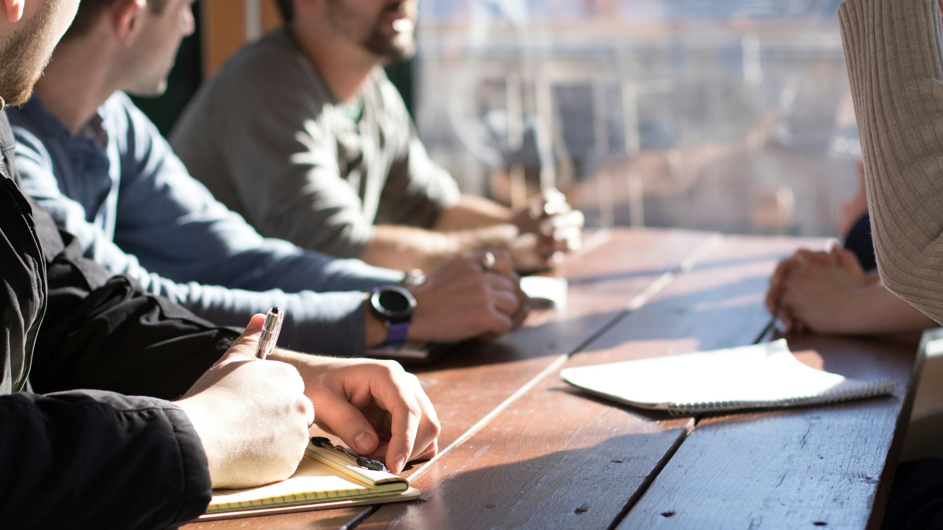 people sitting on chair in front of table while holding pens during daytime