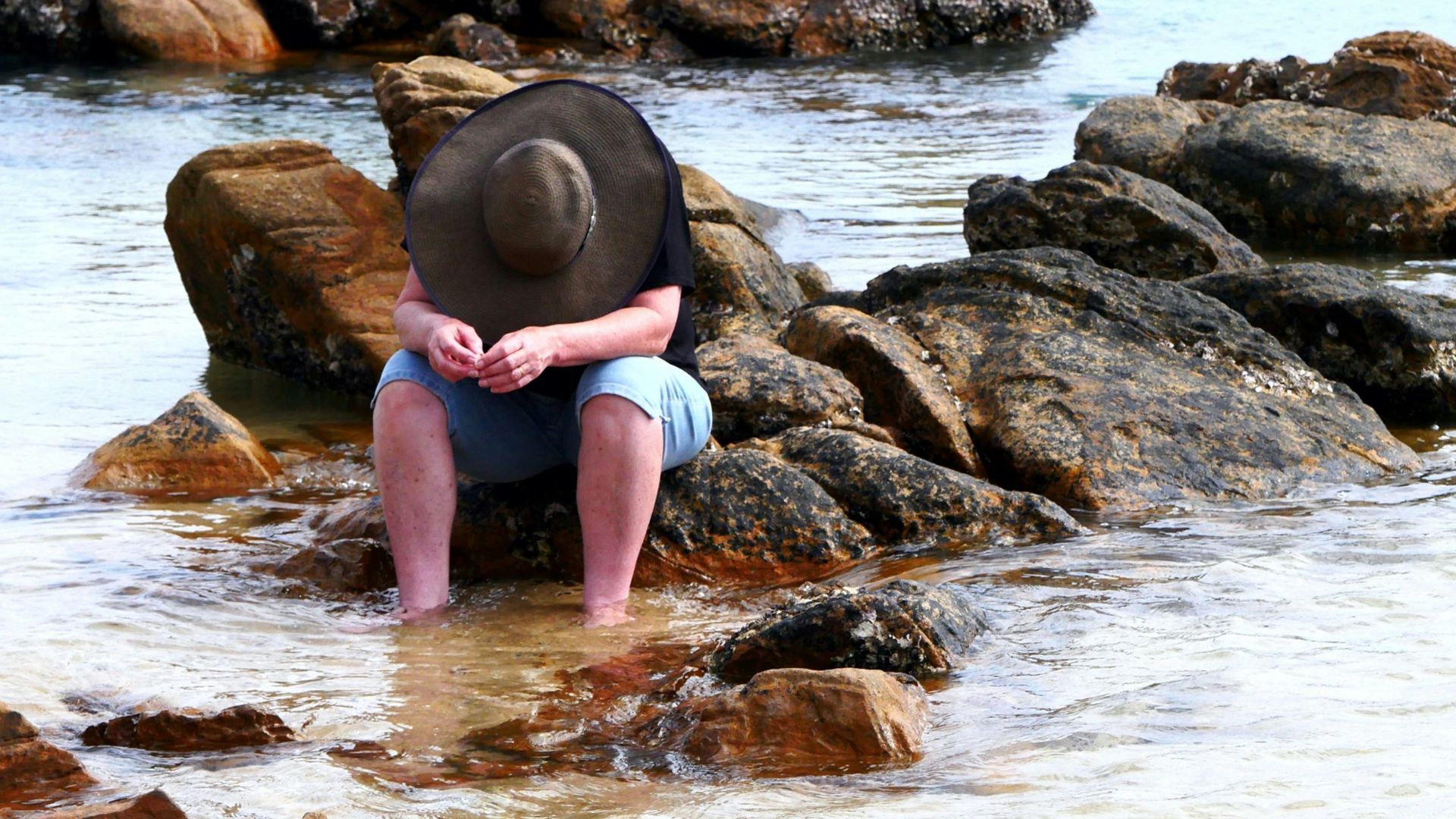 woman in pink shirt sitting on rock in the sea