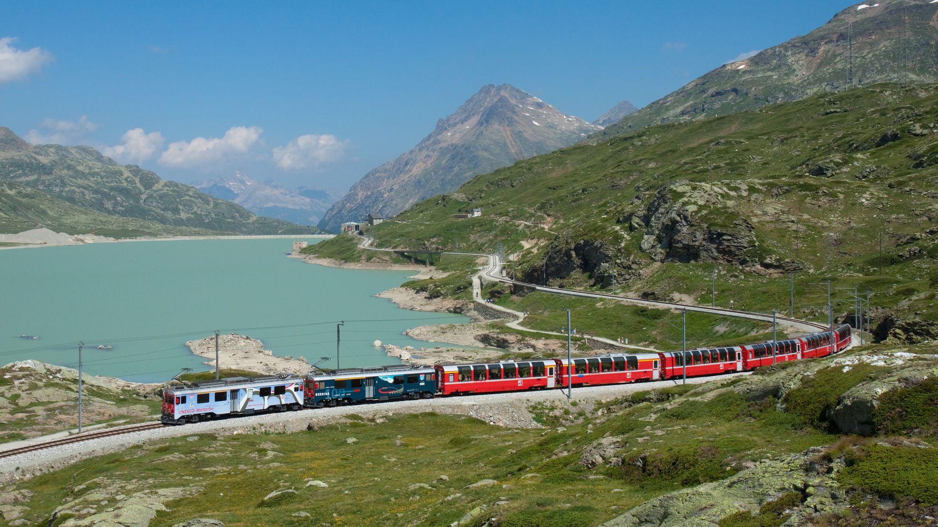 Two RhB ABe 4/4III motor coaches in multiple unit with a Bernina Express train on the Bernina line, passing Lago Bianco.