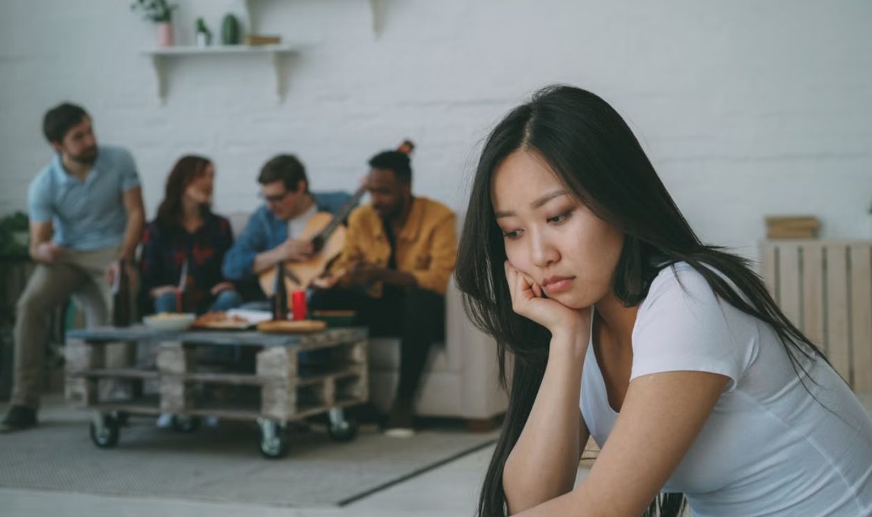 Young woman looks lonely at a party while others socialize in the background