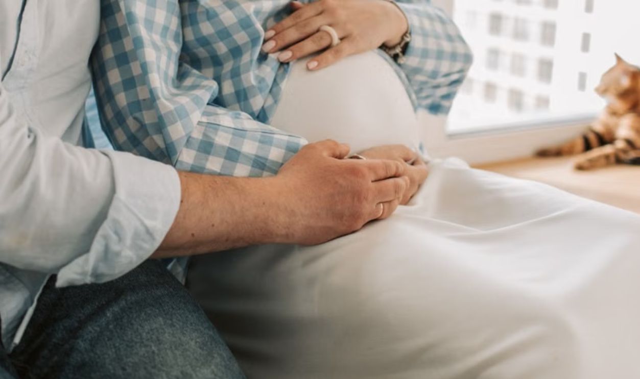 A couple enjoy a tender moment with their baby bump at home, featuring a cute cat
