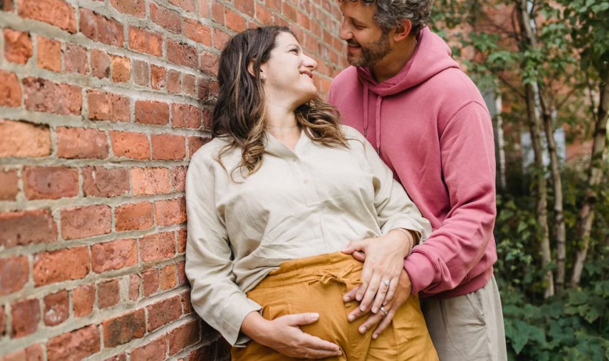 A joyful couple embracing while expecting a baby, standing by a brick wall outdoors