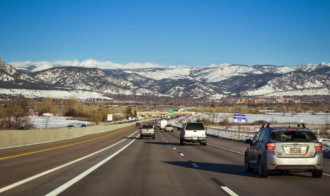 A scenic highway view surrounded by snow-capped mountains under a clear blue sky, showcasing traffic flow in Colorado