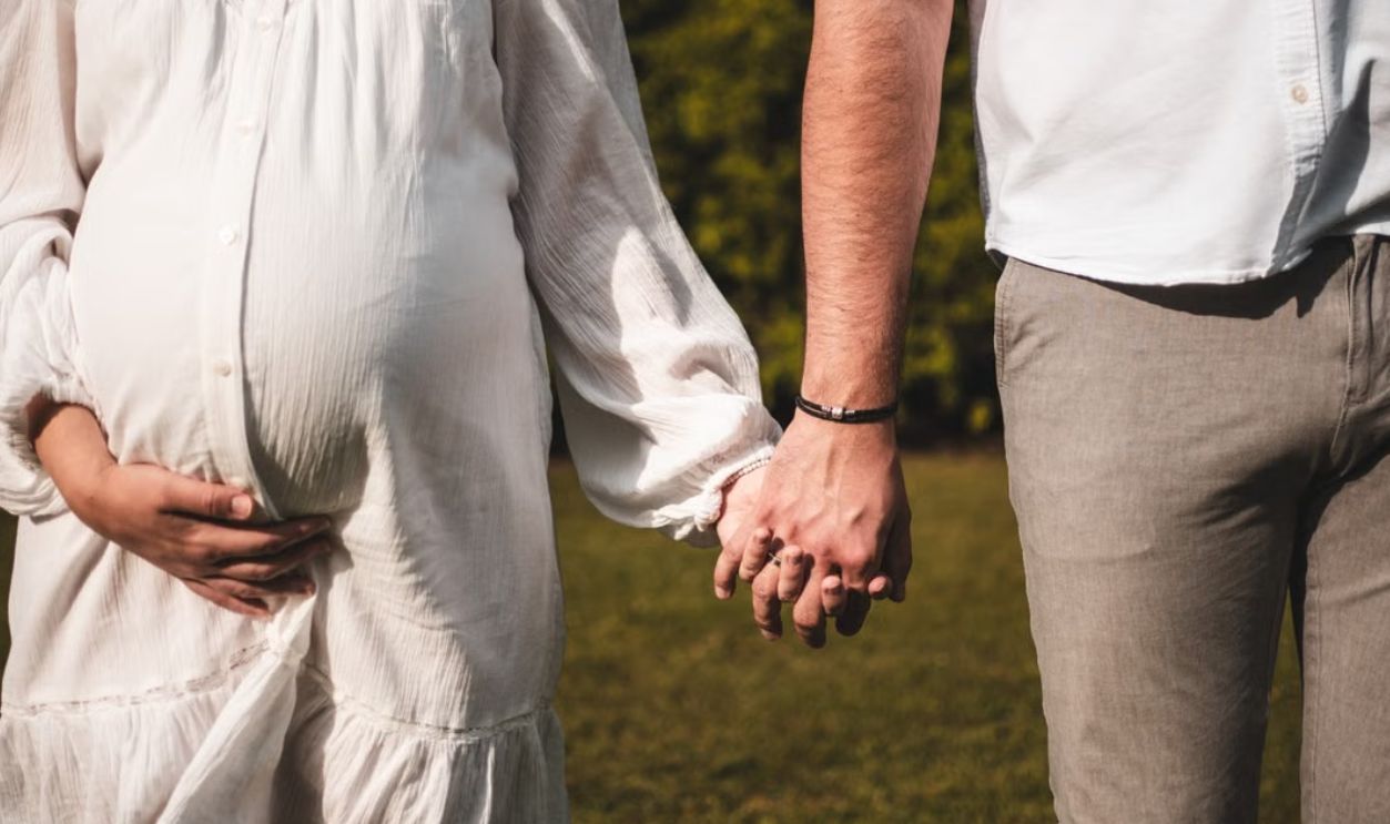 A pregnant woman and man holding hands outdoors, symbolizing love and family