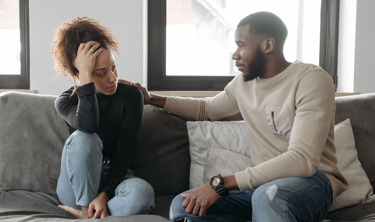A couple shares a moment on their sofa at home, conveying care 