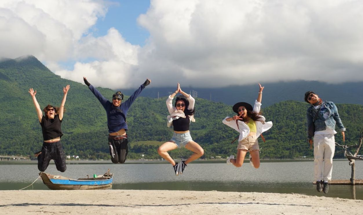 Five friends jumping joyfully on a beach with mountains and clouds in the background