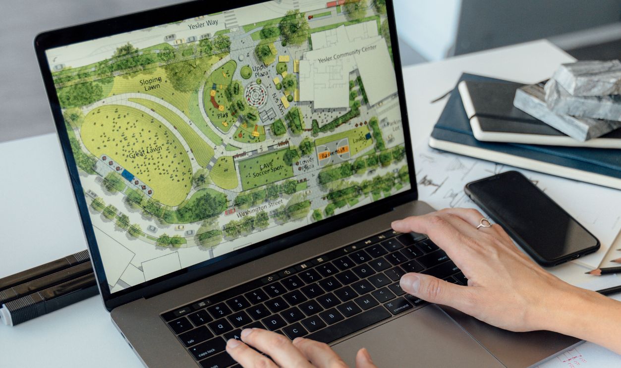 Architect working on landscape plan displayed on laptop with hands typing on keyboard.