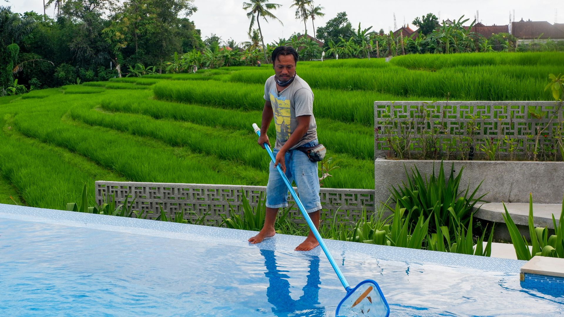 man in white polo shirt and blue denim jeans standing on swimming pool during daytime